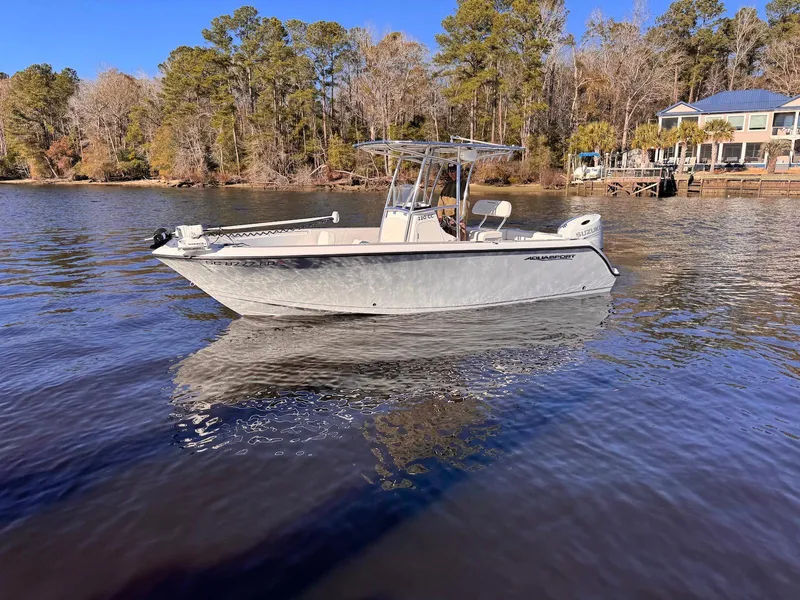 Slide: The Image of 2024 Aquasport 2200 Center Console boat on a calm lake near a wooded shoreline. - 3