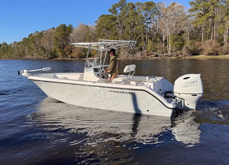 Slide: The Image of 2024 Aquasport 2200 Center Console boat on a calm lake with trees in the background. - 4
