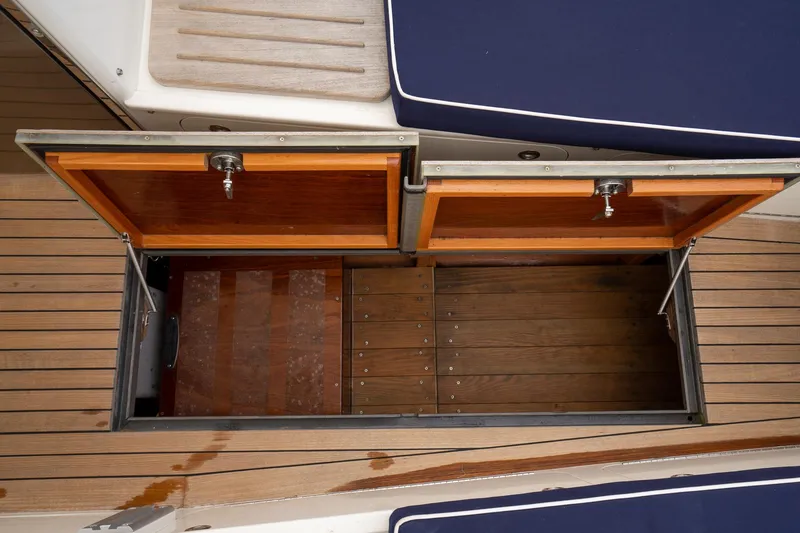 Slide: The Image of Open storage compartment on 2021 Brooklin Boat Yard 32 Express, featuring wooden deck and blue cushions. - 38