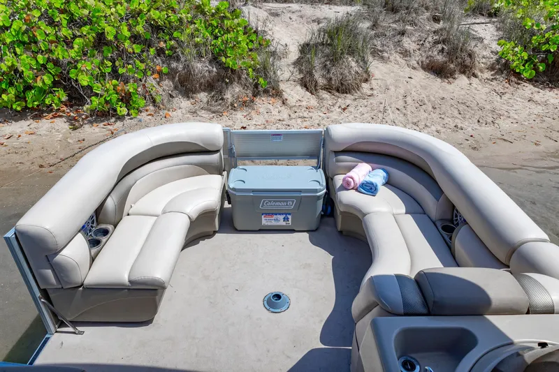 Slide: The Image of 2016 Starcraft 206 Sundeck boat interior with beige seating and cooler on sandy shore. - 2