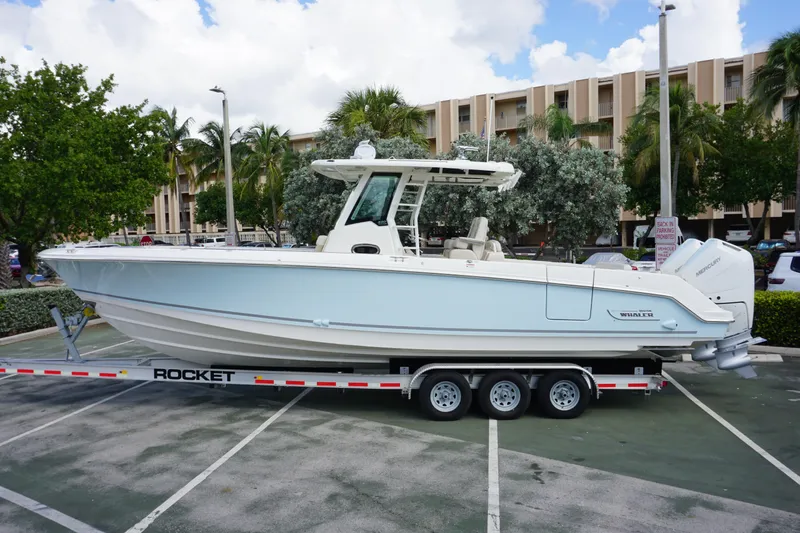 Slide: The Image of 2026 Boston Whaler 330 Outrage boat on trailer in parking lot, surrounded by trees. - 1