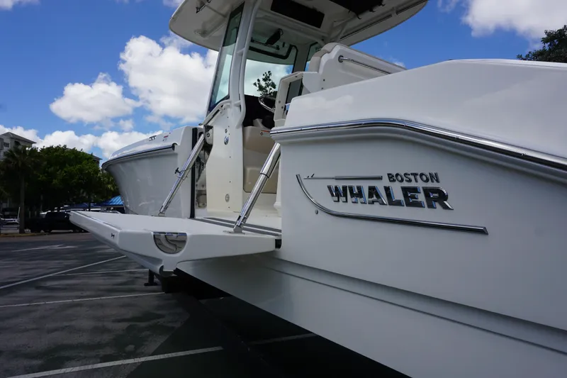 Slide: The Image of 2026 Boston Whaler 280 Dauntless boat, side view with logo, parked under blue sky. - 44