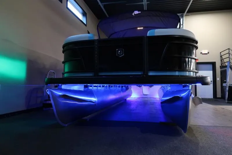Slide: The Image of 2025 Sweetwater SW 2286 QS pontoon boat with blue underglow lighting in a showroom. - 23
