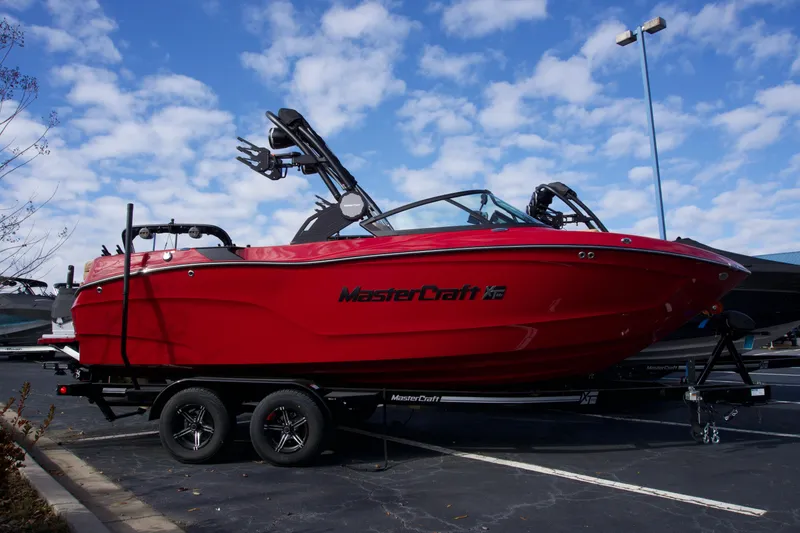 The Image of 2025 MasterCraft XT22T boat in vibrant red on a trailer under a blue sky. - 0