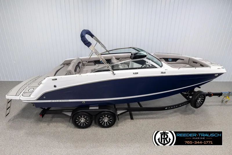 The Image of 2025 Four Winns HD5 boat on trailer, blue and white design, displayed indoors. - 1