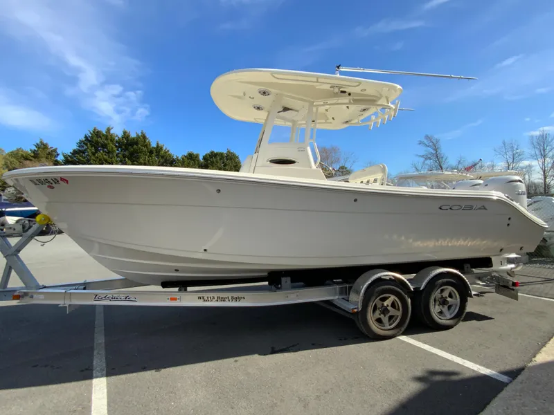 Slide: The Image of 2024 Cobia 240 Center Console boat on trailer, parked outdoors under blue sky. - 6