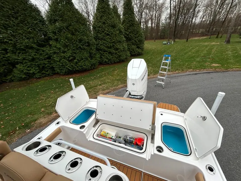 Slide: The Image of 2025 Caymas 26 HB boat with open storage compartments and outboard motor, parked near trees. - 39