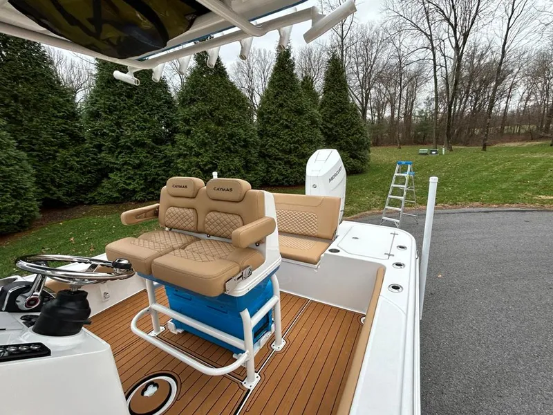 Slide: The Image of 2025 Caymas 26 HB boat with tan seating and wood deck, parked near trees. - 49