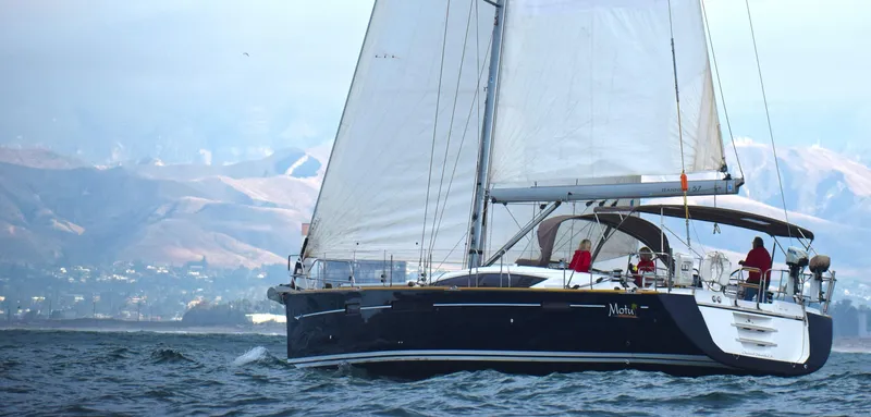 Slide: The Image of 2013 Jeanneau 57 sailboat cruising on open water with mountains in the background. - 0