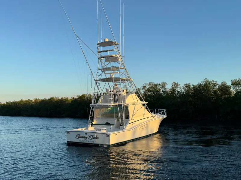 Slide: The Image of Cabo 45 Express 1999 yacht on calm water at sunset, surrounded by trees. - 5