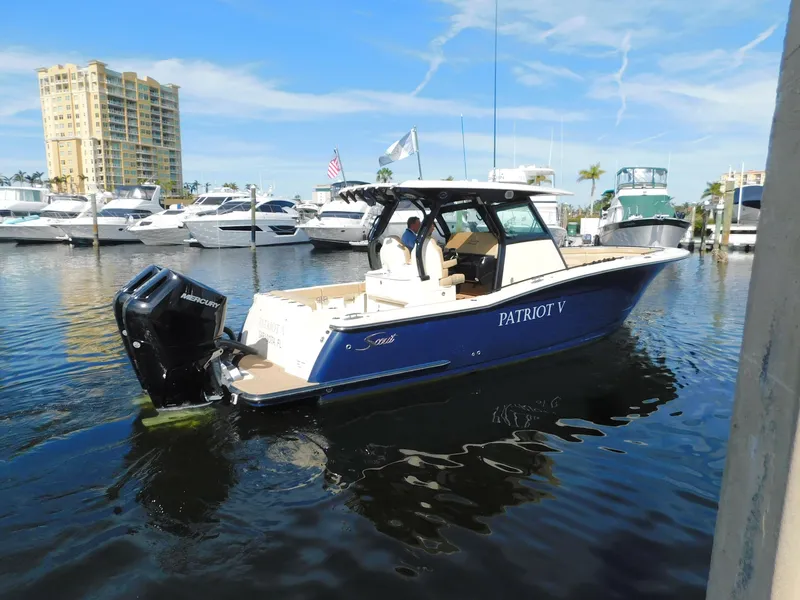 Slide: The Image of 2024 Scout 33LXF boat docked in marina, blue hull, outboard engines, clear sky. - 3