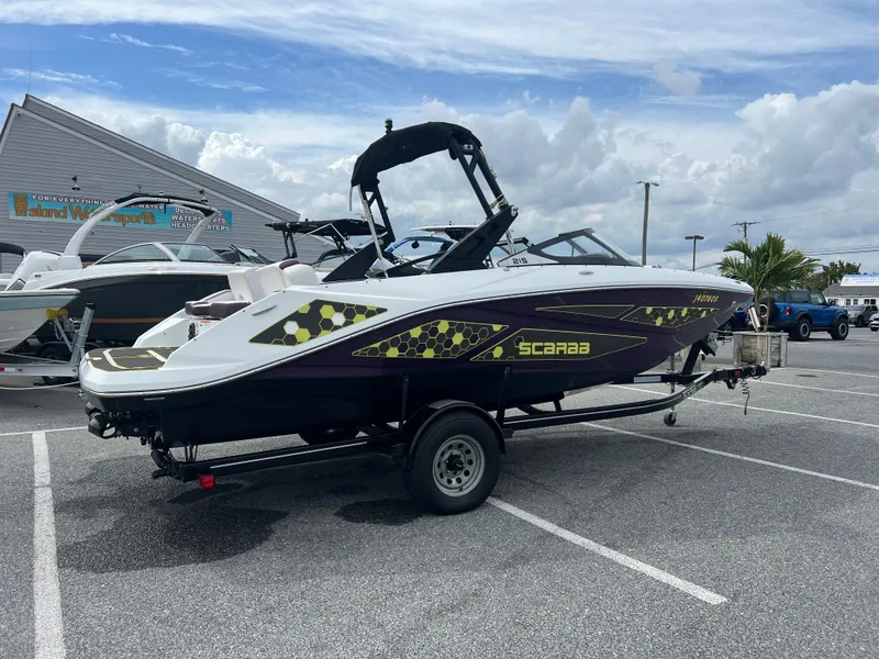 Slide: The Image of 2020 Scarab 215ID boat on trailer in parking lot, cloudy sky background. - 2