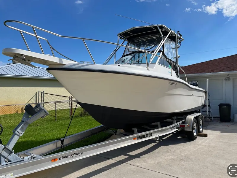 Slide: The Image of 1995 Pursuit 2470 boat on trailer, parked in driveway under clear blue sky. - 10