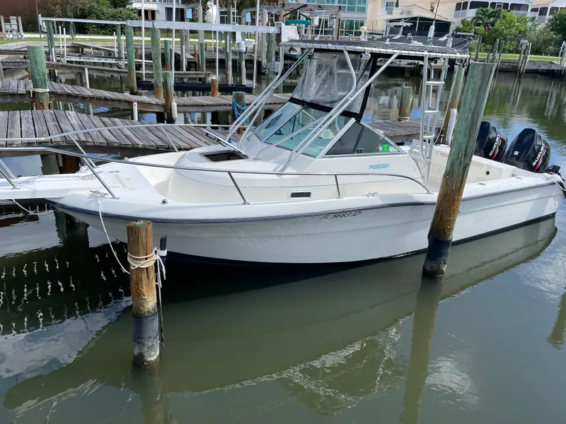 Slide: The Image of 1995 Pursuit 2470 boat docked in a marina, featuring dual outboard motors. - 2