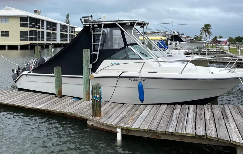 Slide: The Image of 1995 Pursuit 2470 boat docked at marina with protective cover and calm waters. - 8