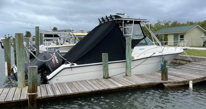 Slide: The Image of 1995 Pursuit 2470 boat docked with Suzuki outboard motor, covered in black tarp. - 9