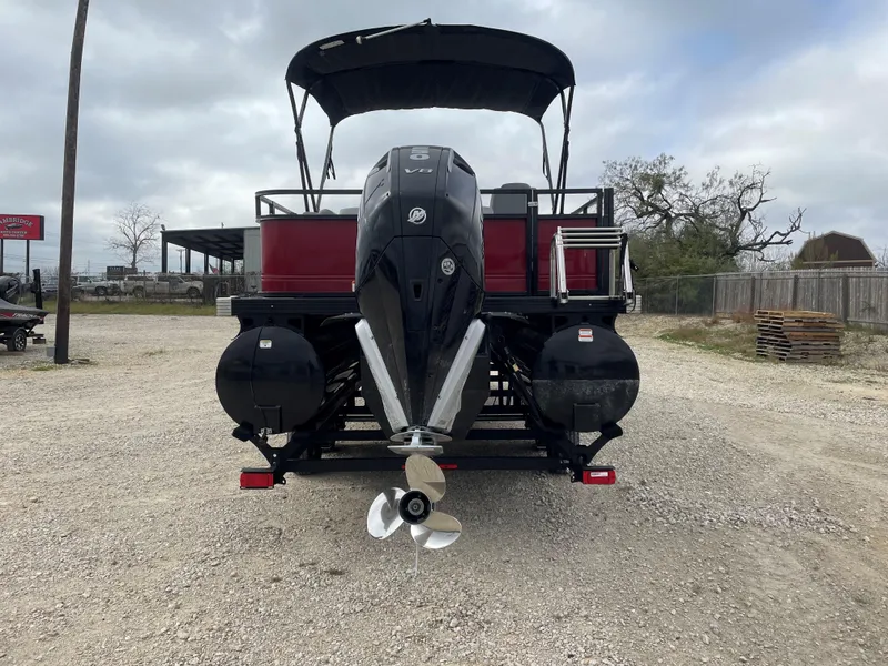 Slide: The Image of 2023 Regency 250 DL3 pontoon boat with outboard motor, parked on gravel. - 3