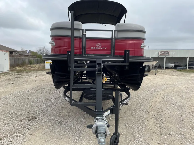 Slide: The Image of 2023 Regency 250 DL3 pontoon boat on trailer, parked on gravel lot. - 7