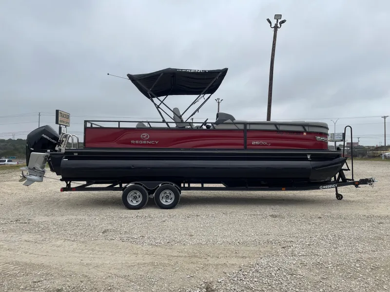 The Image of 2023 Regency 250 DL3 pontoon boat on trailer, red and black design, parked outdoors. - 0