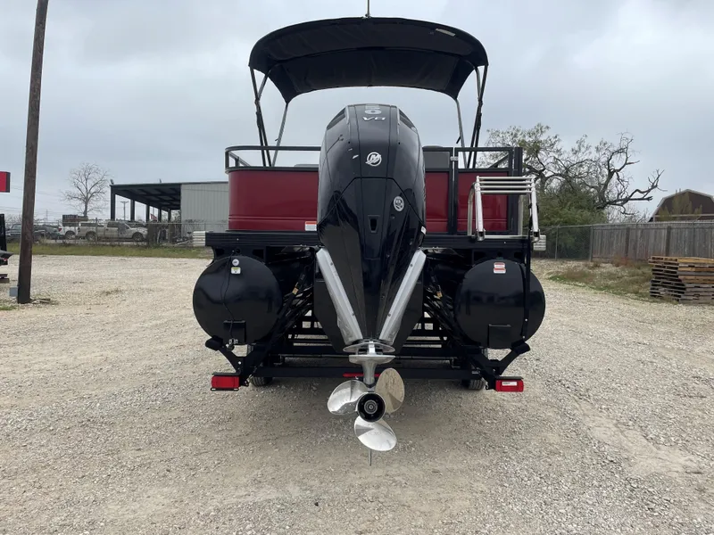 Slide: The Image of 2023 Regency 250 DL3 pontoon boat with powerful outboard motor, parked on gravel. - 2