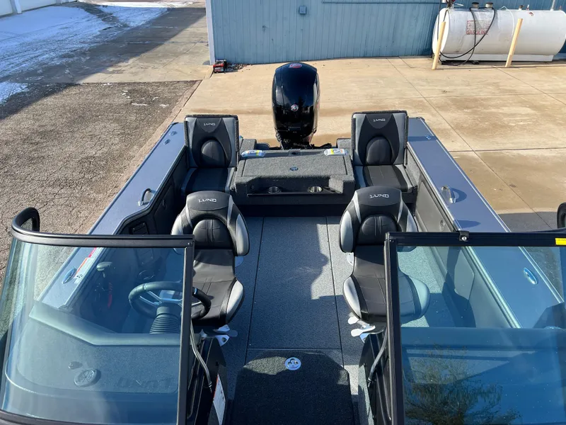 Slide: The Image of 2025 Lund 1875 Pro-V boat interior with seating and motor, parked on concrete. - 22