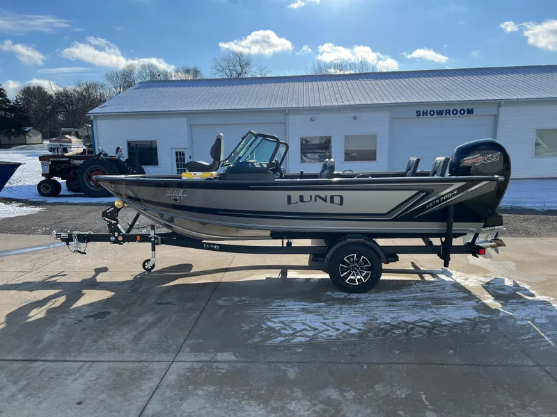 Slide: The Image of 2025 Lund 1875 Pro-V boat on trailer outside showroom under blue sky. - 3