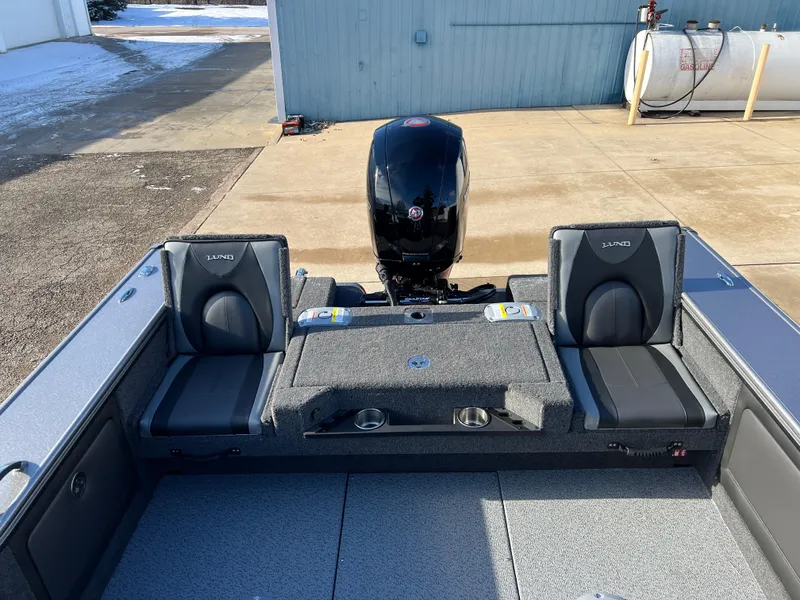 Slide: The Image of 2025 Lund 1875 Pro-V boat interior with seating and motor, parked on concrete. - 36