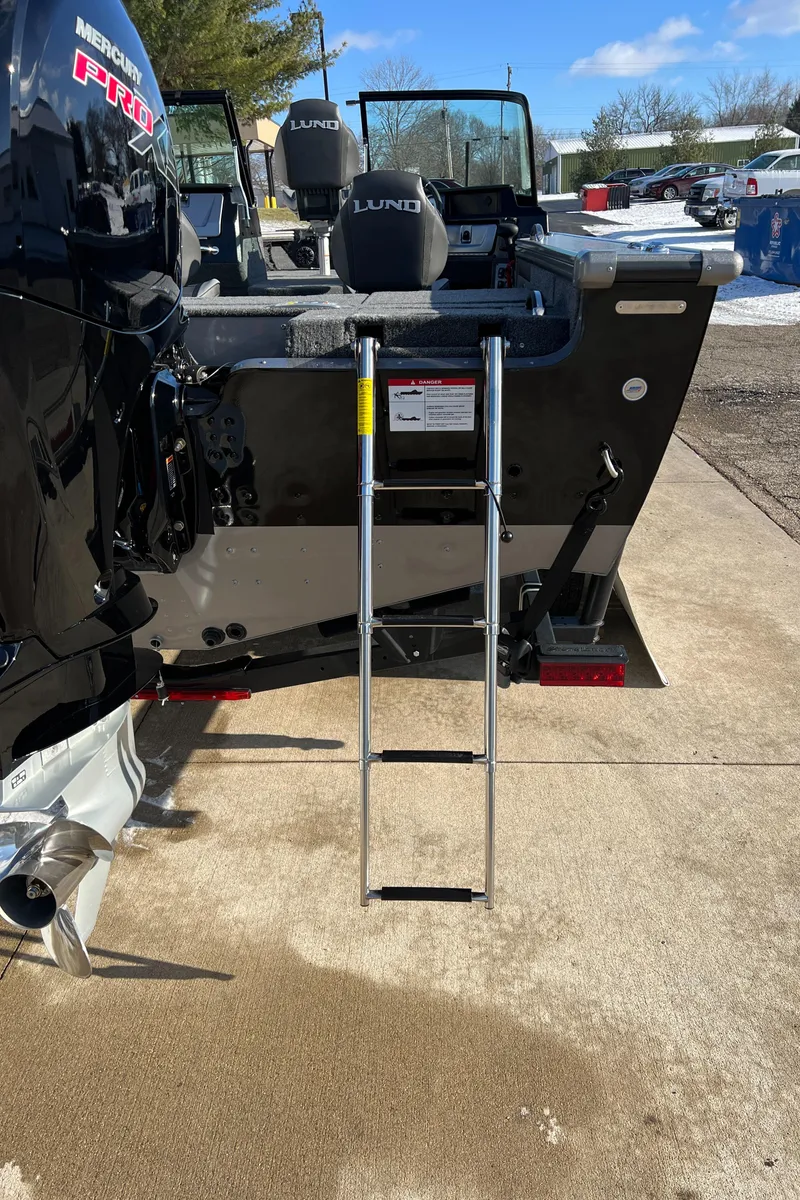 Slide: The Image of 2025 Lund 1875 Pro-V boat with ladder, parked on concrete under clear sky. - 7