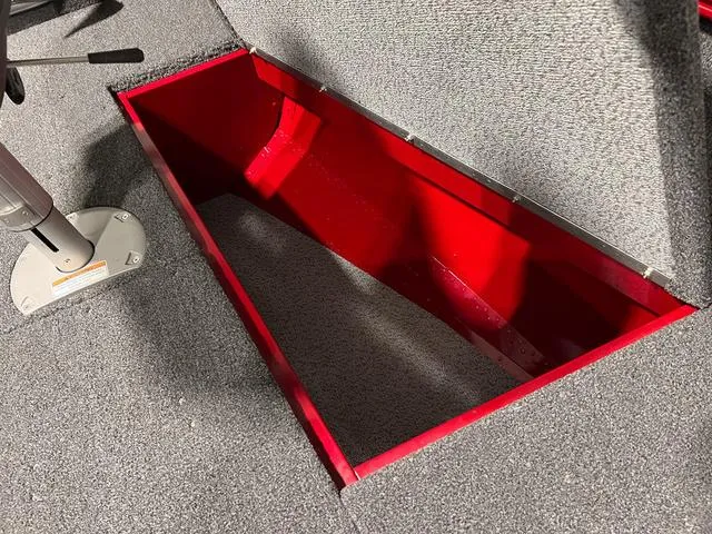 Slide: The Image of 2024 Lund 1775 Pro Guide Tiller storage compartment with red interior and gray carpet. - 14