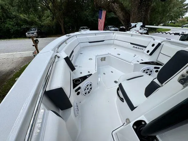 Slide: The Image of 2021 Blackfin 252 CC boat interior with seating and speakers, parked near trees and road. - 26