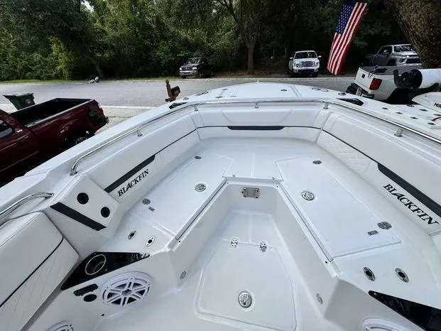 Slide: The Image of 2021 Blackfin 252 CC boat interior with seating and storage, parked near trees and vehicles. - 28