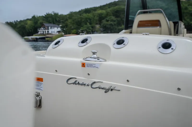 Slide: The Image of 2024 Chris-Craft Calypso 32 boat, rear view with logo, near a lakeside house. - 19