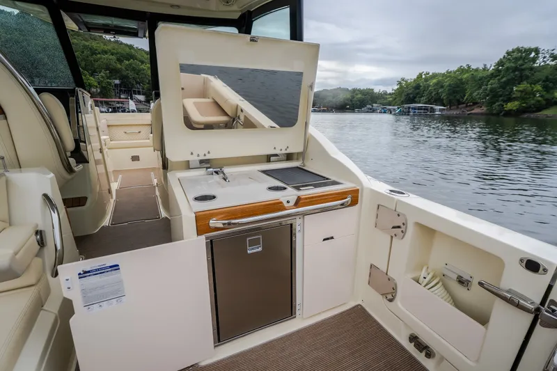 Slide: The Image of 2024 Chris-Craft Calypso 32 boat interior with kitchenette, overlooking serene lake and lush greenery. - 27