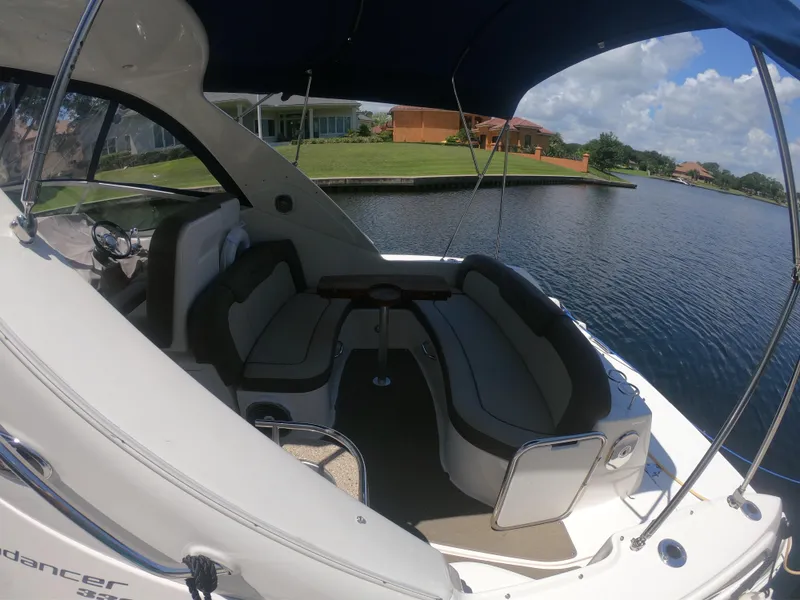 Slide: The Image of 2015 Sea Ray 330 Sundancer boat interior with seating, docked by a scenic waterfront. - 4