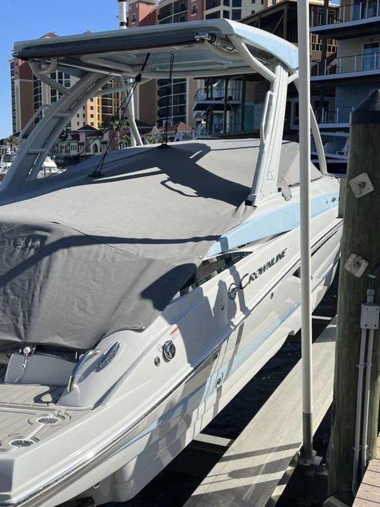 Slide: The Image of 2025 Crownline 290 XSS boat docked, covered, with modern architecture in the background. - 3