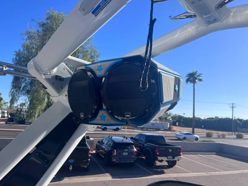 Slide: The Image of Centurion Ri265 2022 boat speakers mounted on a wakeboard tower, sunny day, parking lot view. - 7
