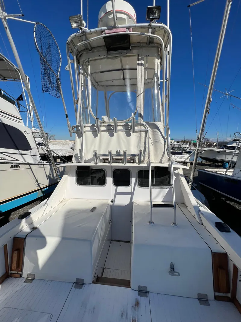 Slide: The Image of 1973 Bertram 31 Flybridge Cruiser with white exterior, docked at a marina under clear blue skies. - 18