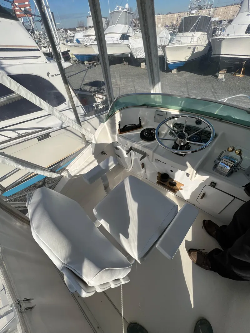Slide: The Image of 1973 Bertram 31 Flybridge Cruiser helm with white seating and steering wheel, docked among boats. - 36