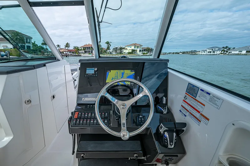Slide: The Image of 2023 Pursuit DC 295 Dual Console helm with navigation system, steering wheel, and waterfront view. - 16