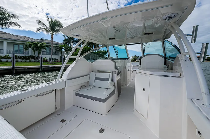 Slide: The Image of 2023 Pursuit DC 295 Dual Console boat interior with seating and helm, docked by palm trees. - 30