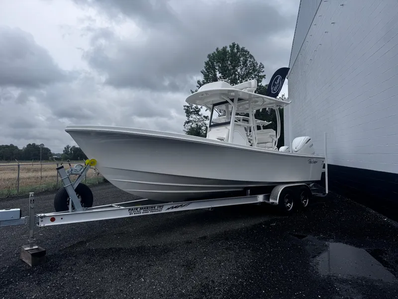 The Image of 2025 Pair Customs 24DV boat on trailer, parked beside a building under cloudy skies. - 1