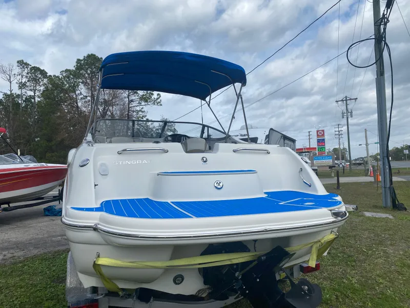 Slide: The Image of 2019 Stingray 250CR boat with blue canopy and deck, parked outdoors. - 2