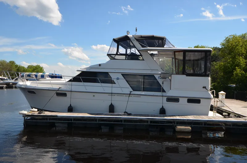 Slide: The Image of 1987 Carver 4207 yacht docked, featuring new canvas and bow thruster, under a clear blue sky. - 4