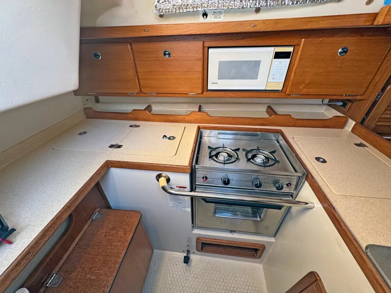 Slide: The Image of Catalina 36 MkII 2000 yacht kitchen with stove, microwave, and wooden cabinetry. - 15