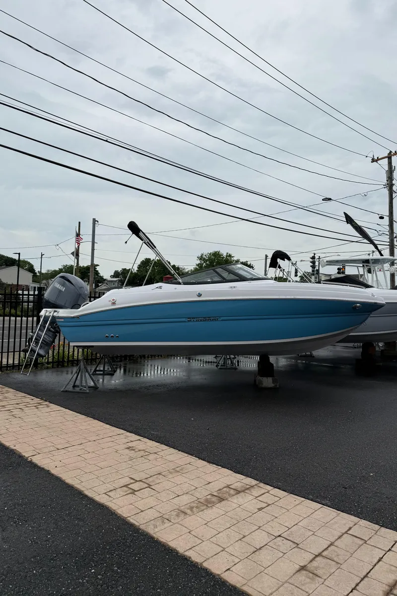 The Image of 2025 Stingray 211 DC boat displayed on stands in a parking lot. - 1