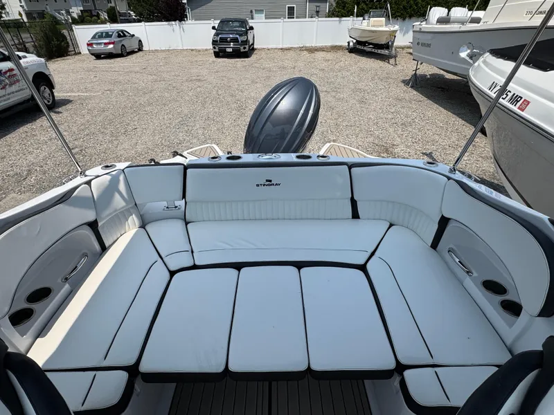 Slide: The Image of 2025 Stingray 211 DC boat interior with white seating, parked in a gravel lot. - 1