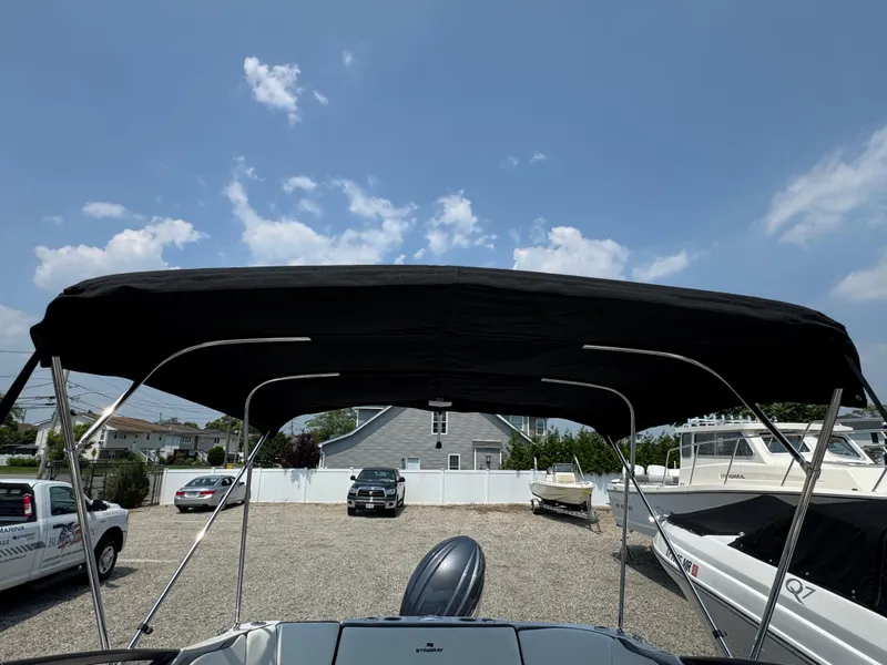 Slide: The Image of 2025 Stingray 211 DC boat with black canopy in a marina setting. - 18