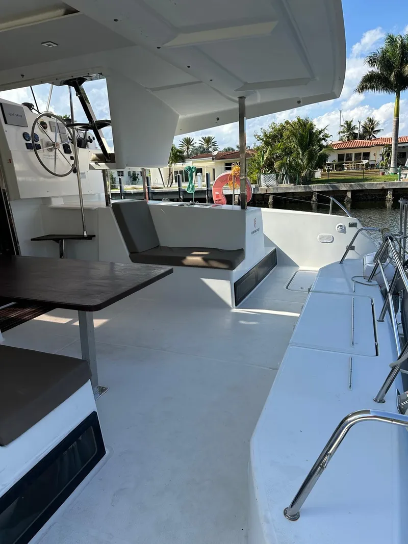 Slide: The Image of 2019 Fountaine Pajot Lucia 40 catamaran with spacious outdoor seating and helm, docked by palm trees. - 32