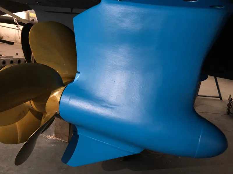 Slide: The Image of Close-up of a 2016 Viking 42 Open boat propeller and rudder, featuring blue and gold colors. - 32