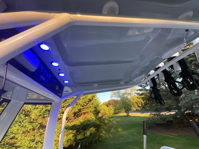 Slide: The Image of 2024 Sea Hunt Ultra 265 SE boat with blue LED lights and canopy, set against a lush landscape. - 22